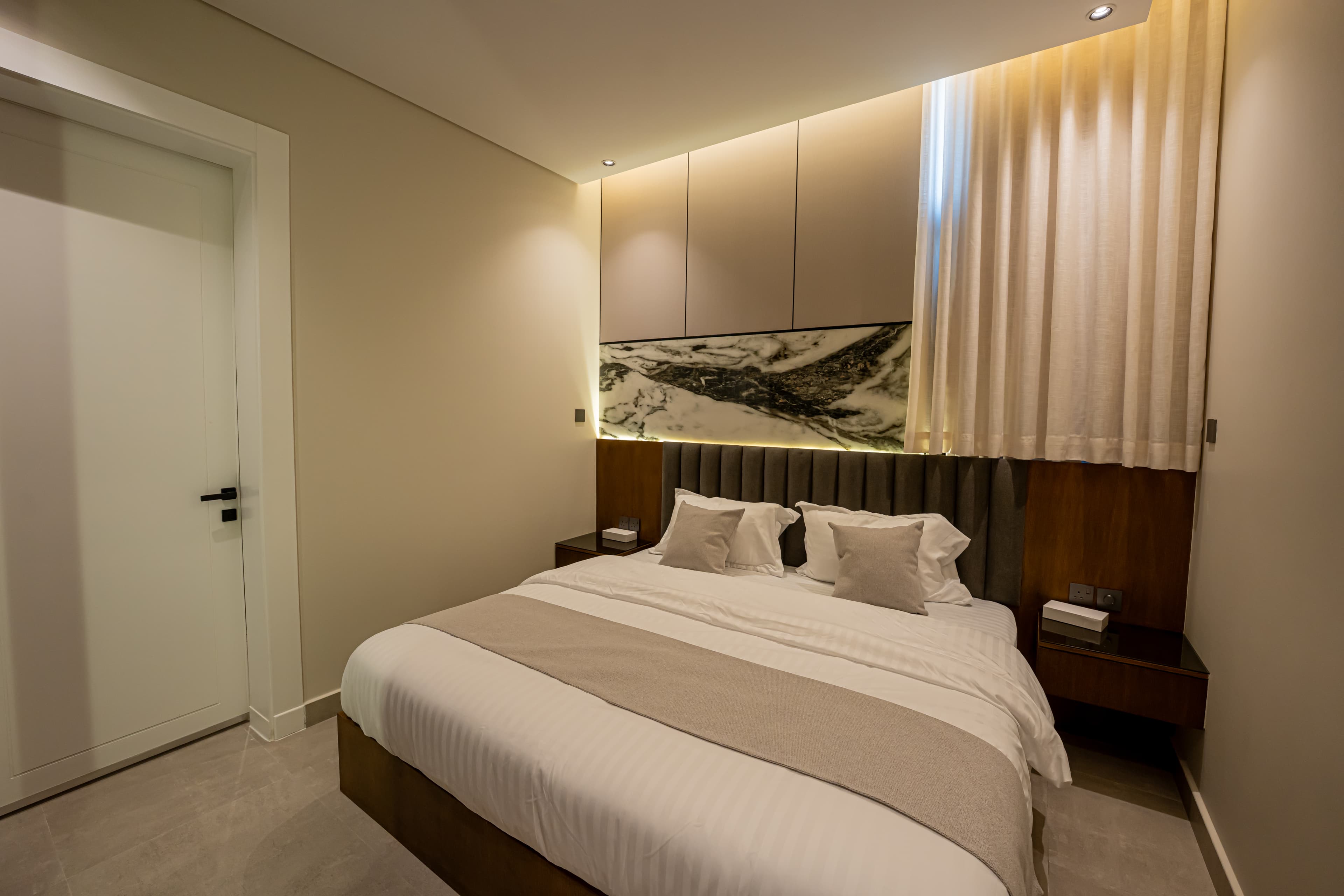 Modern bedroom featuring a marble accent wall, grey headboard, and warm recessed lighting.