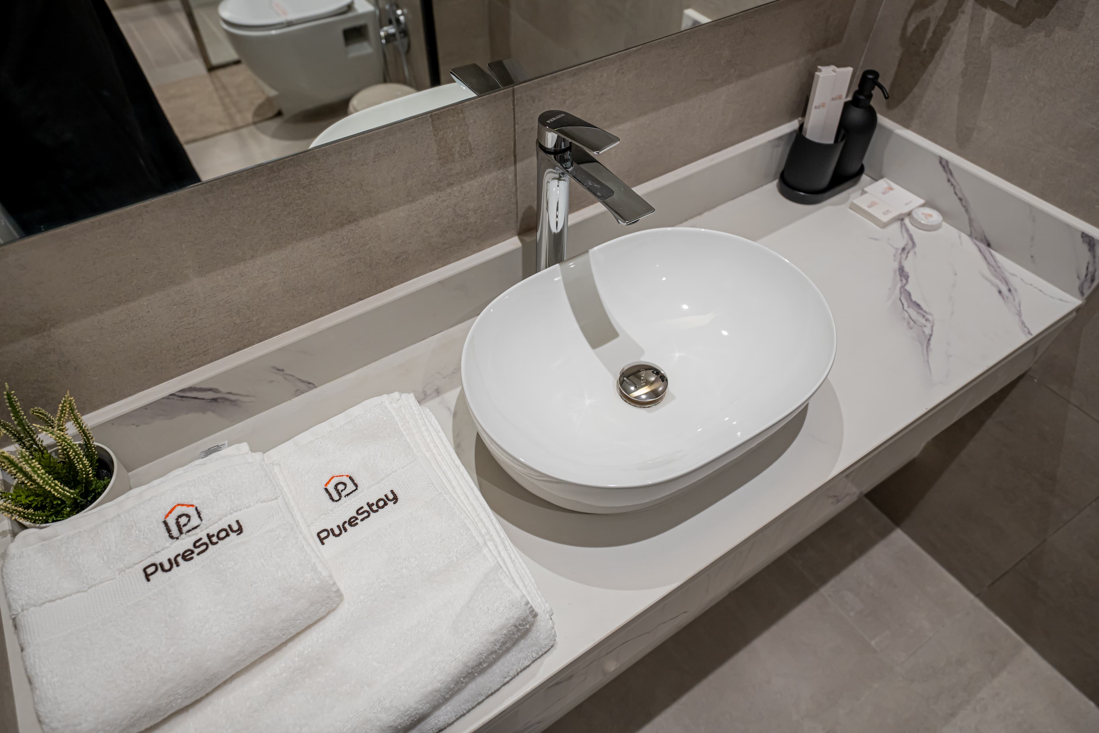 White vessel sink on marble countertop with folded PureStay towels and a small plant.