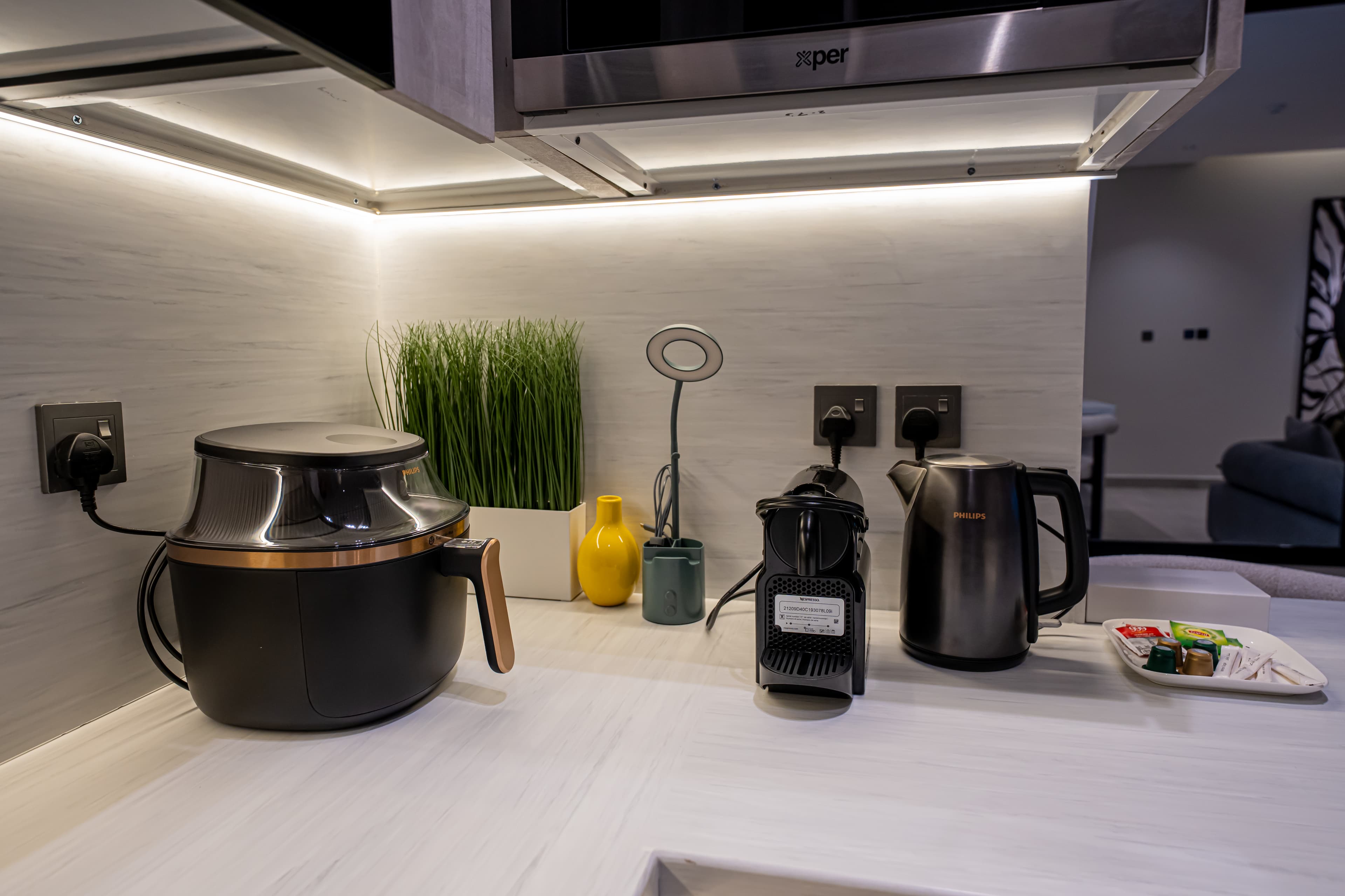 Black air fryer, coffee machine, and kettle on a white countertop under bright cabinet lights.