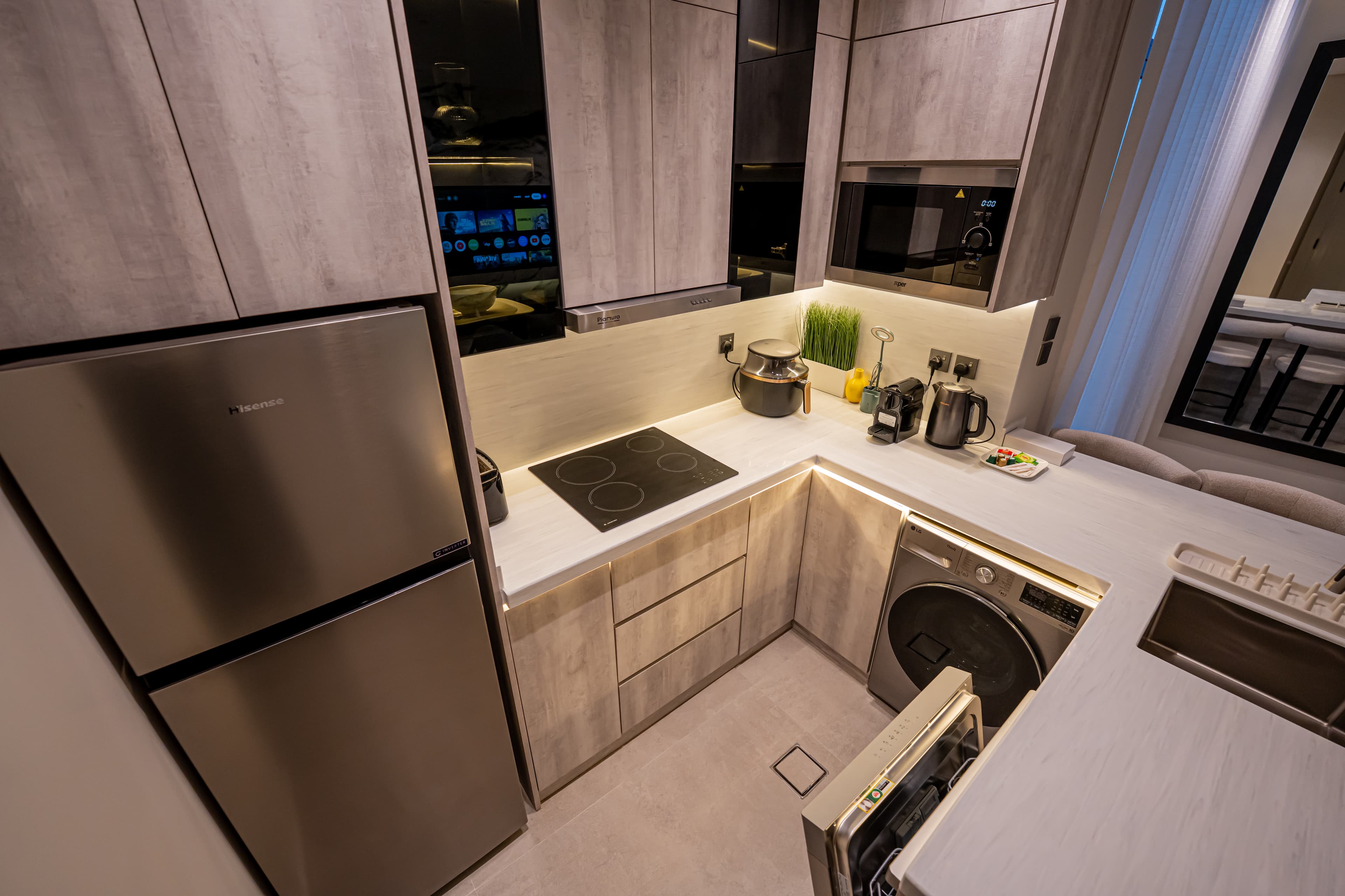 Modern compact kitchen featuring light wood cabinets, stainless steel appliances, and integrated washing machine.